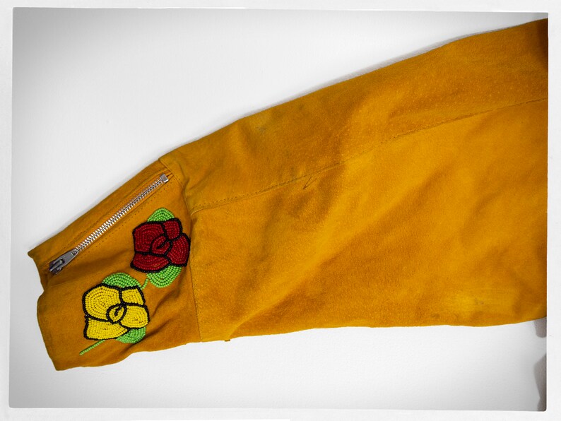 May include: A mustard yellow suede jacket with a zipper detail on the sleeve. The sleeve has a beaded design of two roses, one red and one yellow.
