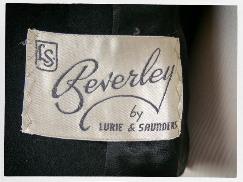 May include: A white label with black text that reads "Beverley by Lurie & Saunders". The label has a small square with the letters "LS" in the top left corner.