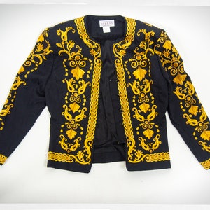 Puede incluir: Una chaqueta negra con bordados dorados con un patr&oacute;n floral. La chaqueta tiene un cuello mandar&iacute;n y un cierre de un solo bot&oacute;n.
