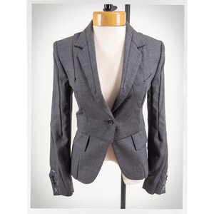 May include: A gray blazer with a single button closure and flap pockets. The blazer has a fitted silhouette and features decorative stitching on the cuffs.
