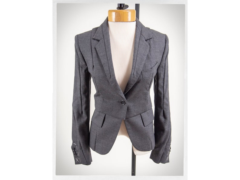 May include: A gray blazer with a single button closure and flap pockets. The blazer has a fitted silhouette and features decorative stitching on the cuffs.