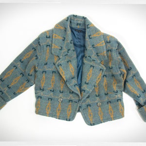 May include: A blue and gold patterned cropped jacket with a double breasted closure and a collar.