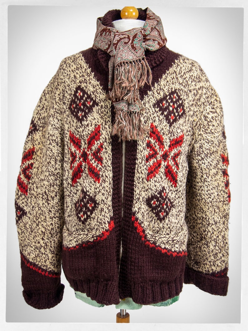 May include: A brown knitted cardigan with a zipper closure and a cream and red geometric pattern. The cardigan has two pockets and is worn with a brown paisley scarf.