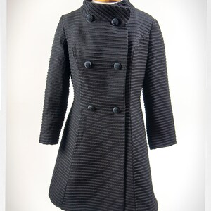 May include: A black double-breasted coat with a high collar and a ribbed texture.