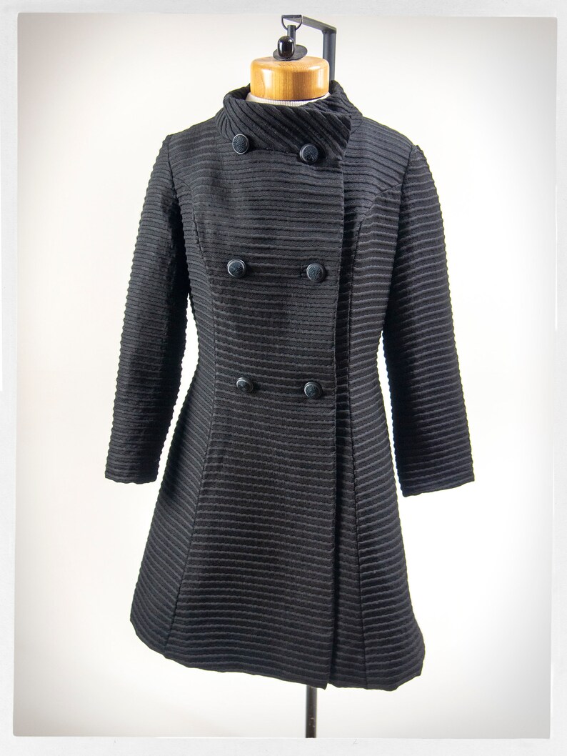May include: A black double-breasted coat with a high collar and a ribbed texture.
