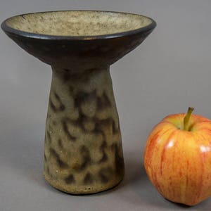 Peut inclure: Un petit vase en c&eacute;ramique brun et beige avec un sommet large et peu profond et une base haute et &eacute;troite. Le vase a une surface marbr&eacute;e et textur&eacute;e.