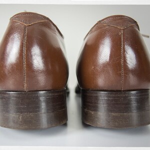 May include: A pair of brown leather dress shoes with a dark brown sole. The shoes are worn and have a slight shine.