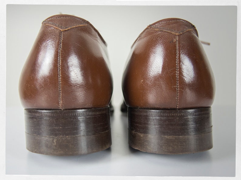 May include: A pair of brown leather dress shoes with a dark brown sole. The shoes are worn and have a slight shine.