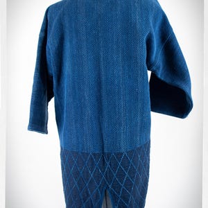 May include: A blue denim jacket with a quilted back panel. The jacket has a relaxed fit and a long length.