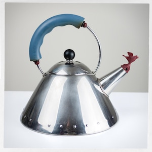May include: A polished stainless steel tea kettle with a conical body and a series of small circular indentations around the base. It features a curved blue handle, a black spherical lid knob, and a red bird-shaped whistle on the spout.