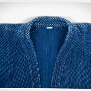 May include: A close-up of a blue denim jacket with a textured weave. The collar is folded down and the jacket is unbuttoned.