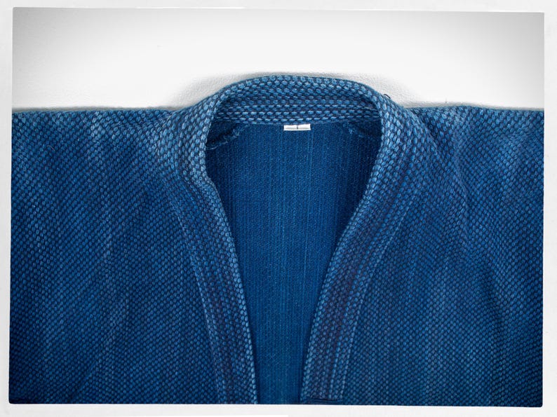 May include: A close-up of a blue denim jacket with a textured weave. The collar is folded down and the jacket is unbuttoned.