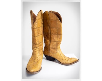 May include: A pair of tan ostrich leather cowboy boots with a pointed toe and a stacked heel.
