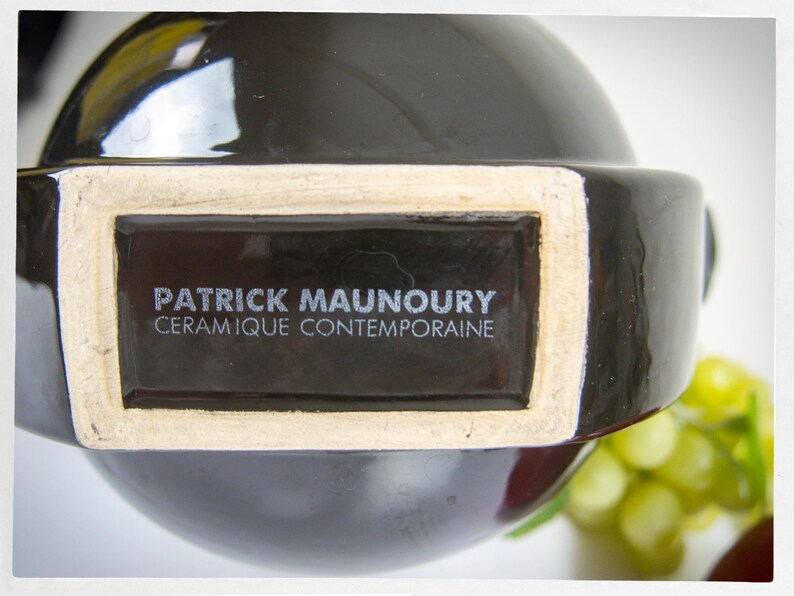 K&ouml;nnte beinhalten: Eine schwarze Keramikvase mit einem wei&szlig;en Etikett, auf dem "Patrick Maunoury, Ceramique Contemporaine" steht.