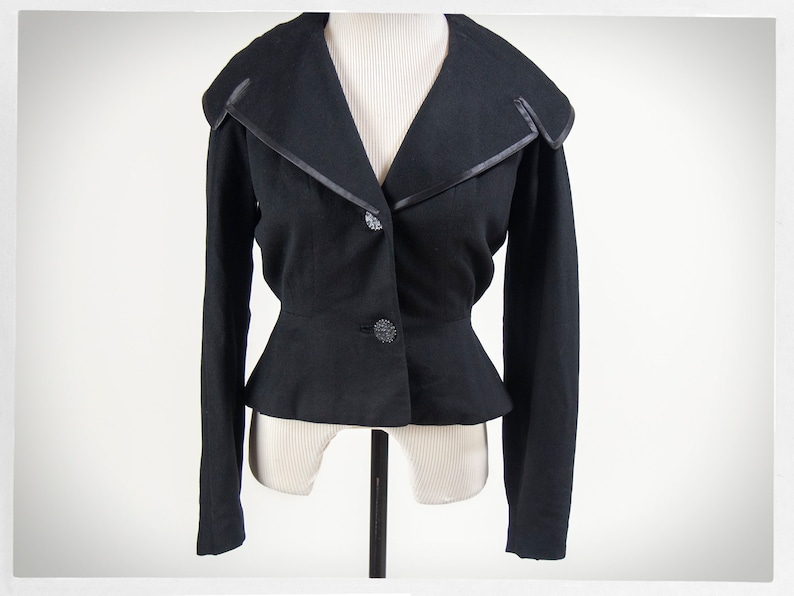 May include: A black cropped jacket with a wide collar and a satin trim. The jacket has a fitted waist and long sleeves.