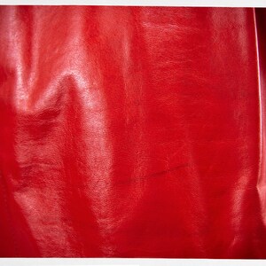 May include: A close-up of a red leather jacket. The leather has a smooth, shiny finish and is slightly wrinkled.