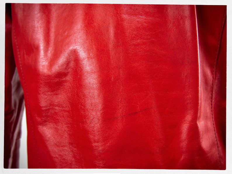May include: A close-up of a red leather jacket. The leather has a smooth, shiny finish and is slightly wrinkled.
