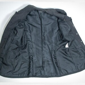 May include: A dark gray wool coat, open to reveal a black satin lining. The coat has a notched collar, button closures, and a tailored fit. The interior features a smooth, dark lining.