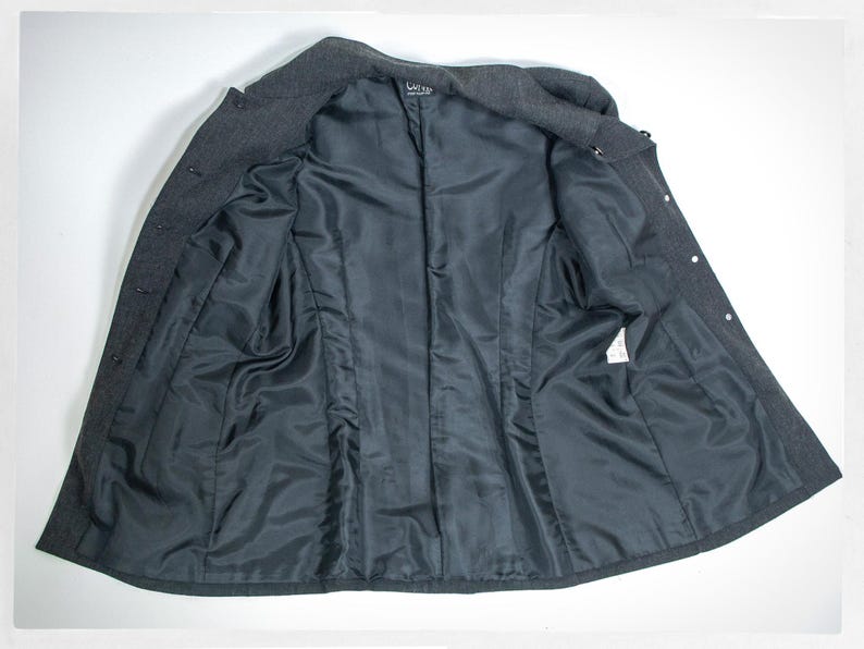 May include: A dark gray wool coat, open to reveal a black satin lining. The coat has a notched collar, button closures, and a tailored fit. The interior features a smooth, dark lining.