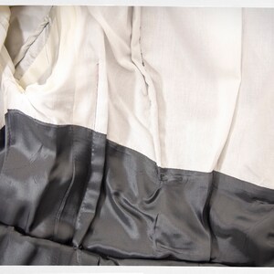 May include: The inside of a black garment with a white lining. The lining is made of a soft, silky fabric. The garment has a seam down the back.