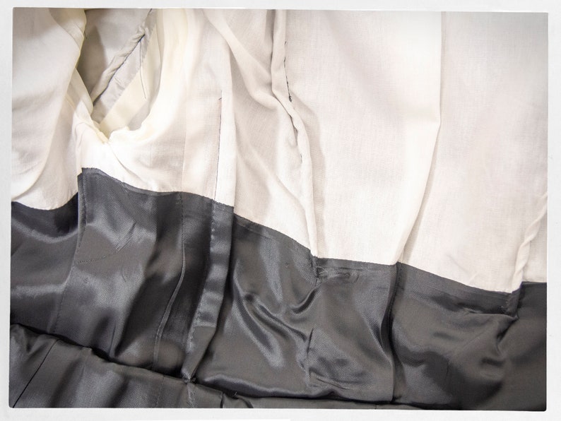 May include: The inside of a black garment with a white lining. The lining is made of a soft, silky fabric. The garment has a seam down the back.