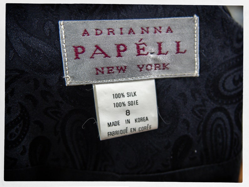 Puede incluir: Un vestido de seda negro con estampado paisley. El vestido tiene una etiqueta que dice "Adrianna Papell New York" y una etiqueta de cuidado que dice "100% Seda, 100% Soie, Hecho en Corea, Fabriqu&eacute; en Cor&eacute;e".