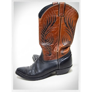 May include: A pair of brown and black cowboy boots with a black leather design on the brown leather shaft.