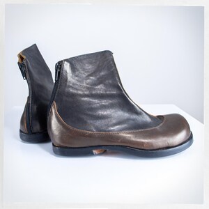 May include: A pair of leather ankle boots. The boots are predominantly black with a brown toe cap and a zip closure at the back. The boots have a rounded toe and a low heel.
