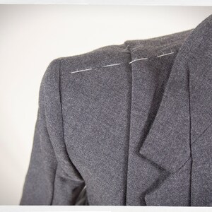 May include: Close-up of a gray blazer with white stitching on the shoulder seam.