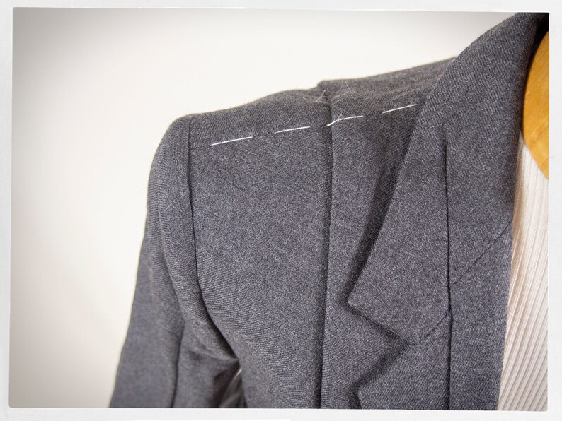 May include: Close-up of a gray blazer with white stitching on the shoulder seam.