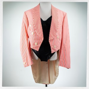 May include: A red and white striped tailcoat with cream-colored buttons and a black bodysuit. The jacket has a double-breasted design and a long, split tail. The outfit is displayed on a mannequin.