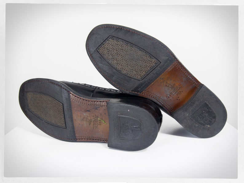 Op de afbeelding: Close-up van de zolen van een paar zwarte leren nette schoenen. De schoenen hebben een textuurrubberen zool en een bruine leren hak.