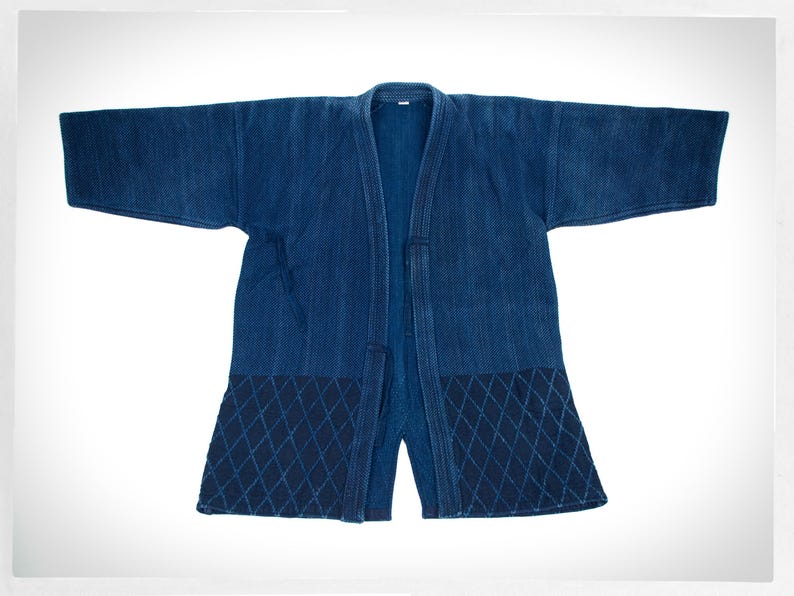 May include: A dark blue indigo Japanese-style jacket with a quilted diamond pattern on the bottom. The jacket is open and has a long, flowing design.