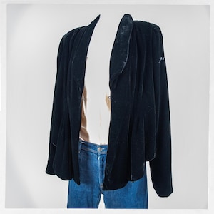 May include: A black velvet jacket with a draped design. The jacket has long sleeves and a unique collar. The garment is paired with blue jeans. The jacket is displayed on a mannequin against a white background.