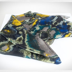May include: A black, blue, yellow, and green patterned silk scarf. The scarf is folded and draped on a white surface.