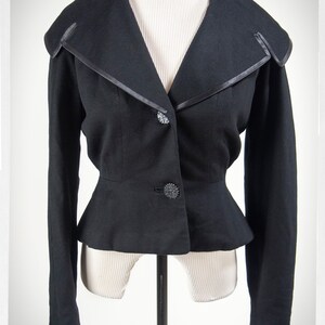 May include: A black cropped blazer with a wide, pointed collar and a fitted waist. The blazer has a satin trim and decorative buttons.