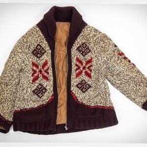 May include: A brown, beige, and red knitted cardigan with a zipper closure and a geometric pattern. The cardigan has a collar and long sleeves.