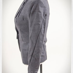 May include: A dark gray blazer with a single button closure and long sleeves. The blazer has a tailored fit and is made of a soft, textured fabric.