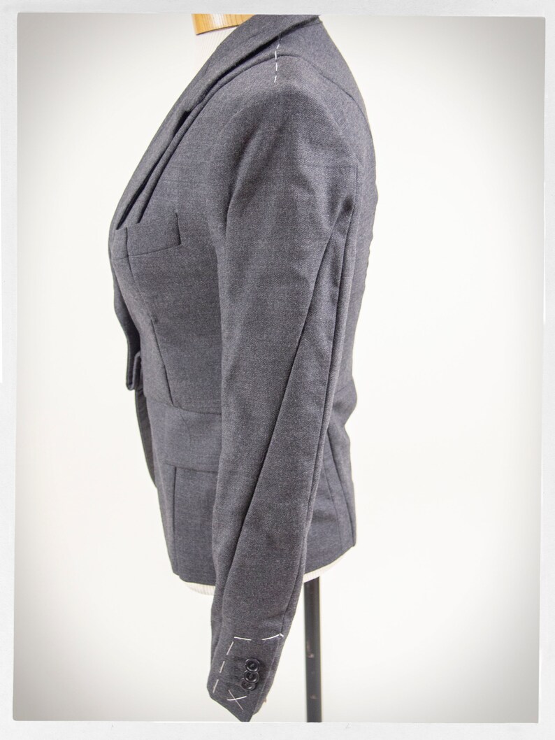 May include: A dark gray blazer with a single button closure and long sleeves. The blazer has a tailored fit and is made of a soft, textured fabric.