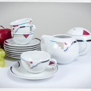 May include: A white tea set with geometric patterns in blue, red, and gray. The set includes a teapot, sugar bowl, and four cups and saucers.
