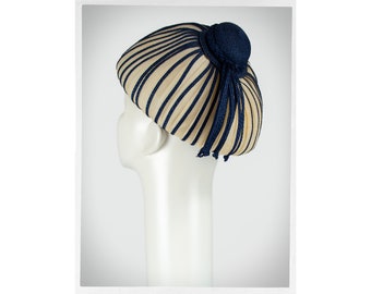 May include: A white and navy blue striped hat with a round, dome-shaped crown and a navy blue topknot. The hat has a long, navy blue tassel hanging from the topknot.