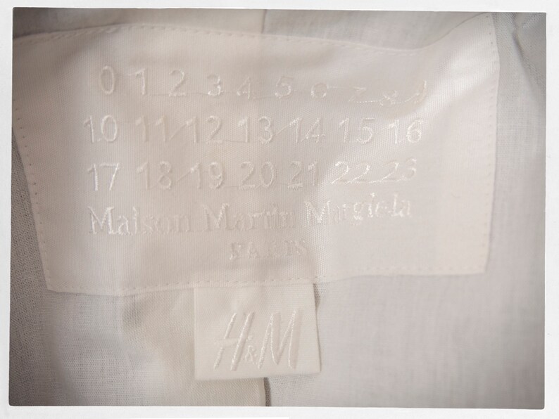 May include: White clothing label with black text that reads "0 1 2 3 4 5 6 7 8 9 10 11 12 13 14 15 16 17 18 19 20 21 22 23 Maison Margiela PARIS" and a white label with black text that reads "H&M".