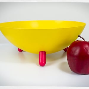 Peut inclure: Un saladier jaune avec trois pieds rouges. Une pomme rouge est à côté du saladier. Le saladier est une pièce d'accent vibrante pour la cuisine ou la salle à manger.