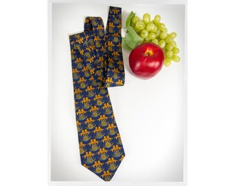 May include: A blue silk tie with a repeating pattern of gold lions. The tie is folded and laid on a white surface with a red apple and green grapes.