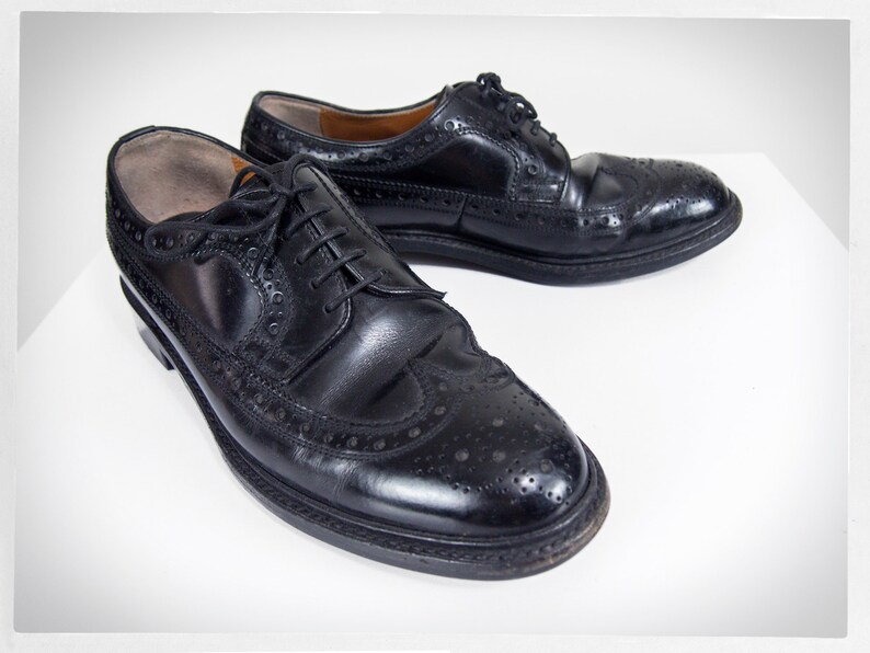 Op de afbeelding: Een paar zwarte leren oxfords met brogue details. De schoenen hebben een vetersluiting en een ronde neus.
