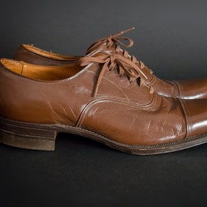 May include: A pair of brown leather lace-up shoes with a cap toe design. The shoes have a polished finish and are in good condition.