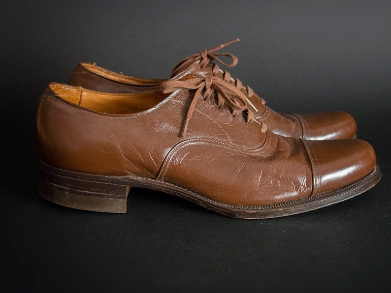 May include: A pair of brown leather lace-up shoes with a cap toe design. The shoes have a polished finish and are in good condition.