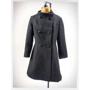 May include: A black, double-breasted coat with a high collar and a ribbed texture. The coat has four buttons down the front.