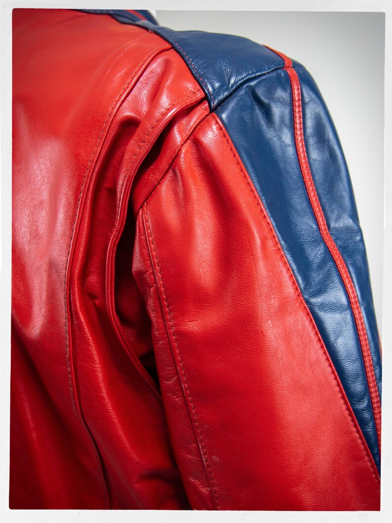 May include: Red leather jacket with blue leather panels and white stitching. The jacket has a sporty look.