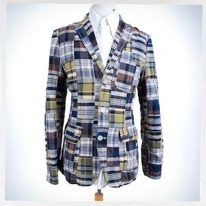 Peut inclure: Blazer patchwork avec différents motifs à carreaux, notamment bleu, vert, marron et blanc. Le blazer a un revers cranté, deux poches avant et trois boutons. Le blazer est présenté sur un mannequin.